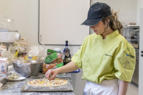 Jeune fille en tenue professionnelle en train de cuisiner une pizza 