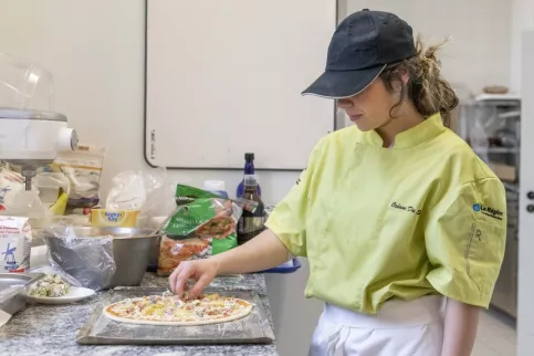 Jeune fille en tenue professionnelle en train de cuisiner une pizza 