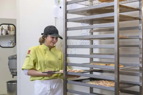 Jeune fille en train de mettre les pizzas sur un chariot